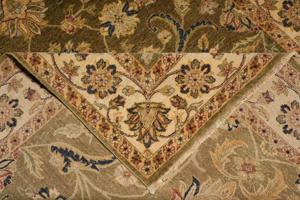 A close-up of an ornate traditional patterned rug or textile shown folded, revealing a cream central field with floral motifs and a border in olive, tan, blue, and rust tones.