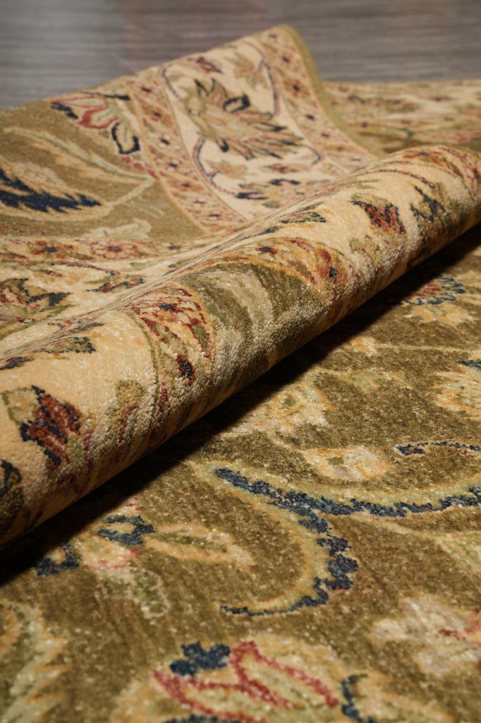 A close-up of a rolled area rug showing its detailed traditional floral and paisley pattern in warm beige, gold, brown, and muted blue tones.