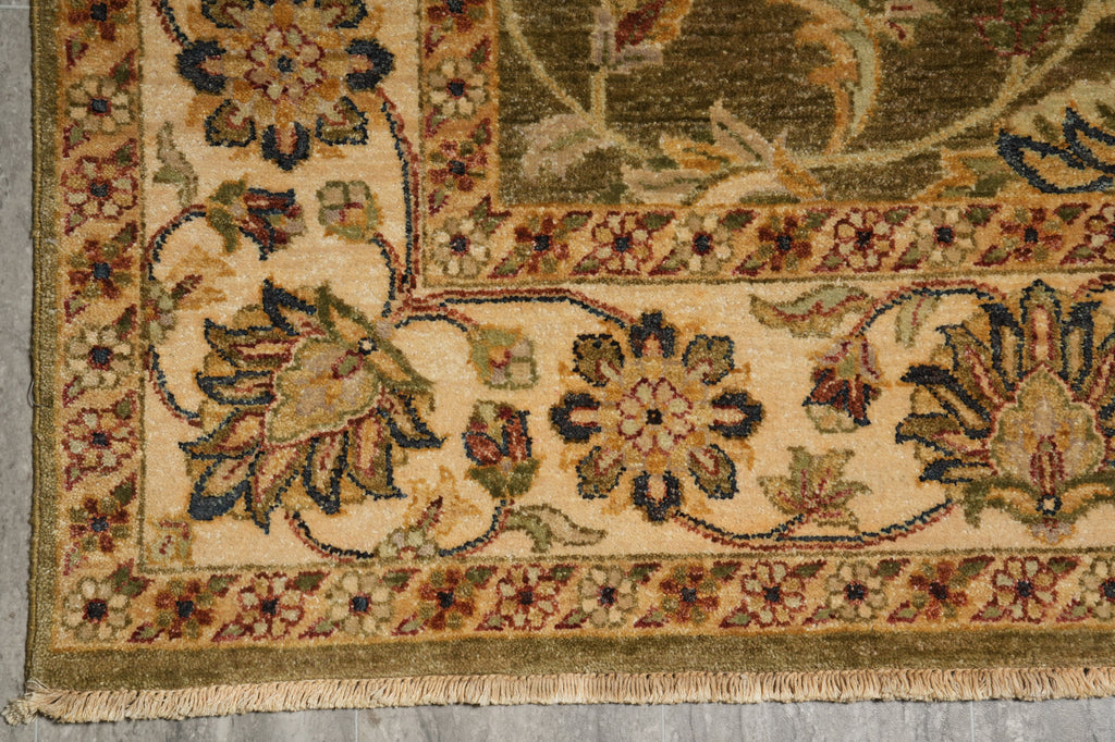 Close-up of an ornate area rug corner showing floral motifs, a decorative border, and fringed edge on a neutral surface.