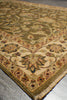 Load image into Gallery viewer, A close-up view of an ornate area rug corner, showing a traditional floral and vine pattern in beige, olive green, brown, and muted red tones with a fringed edge on a gray floor.