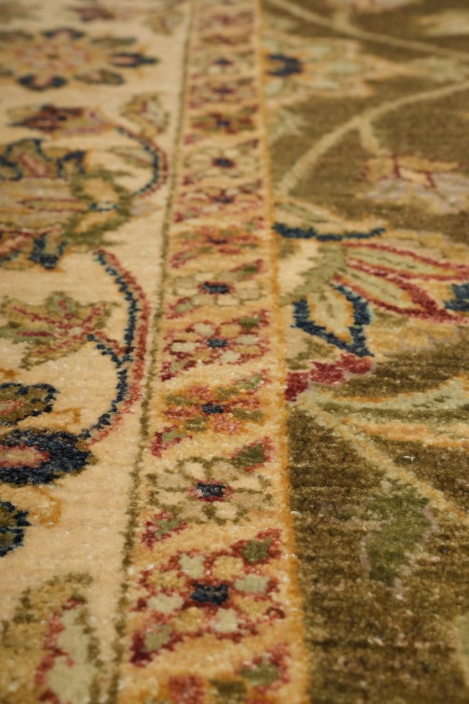 Close-up of a traditional patterned area rug showing a cream central field, a narrow ornate border in beige and rust tones, and a wider olive-green section with floral motifs in blue, red, and cream.