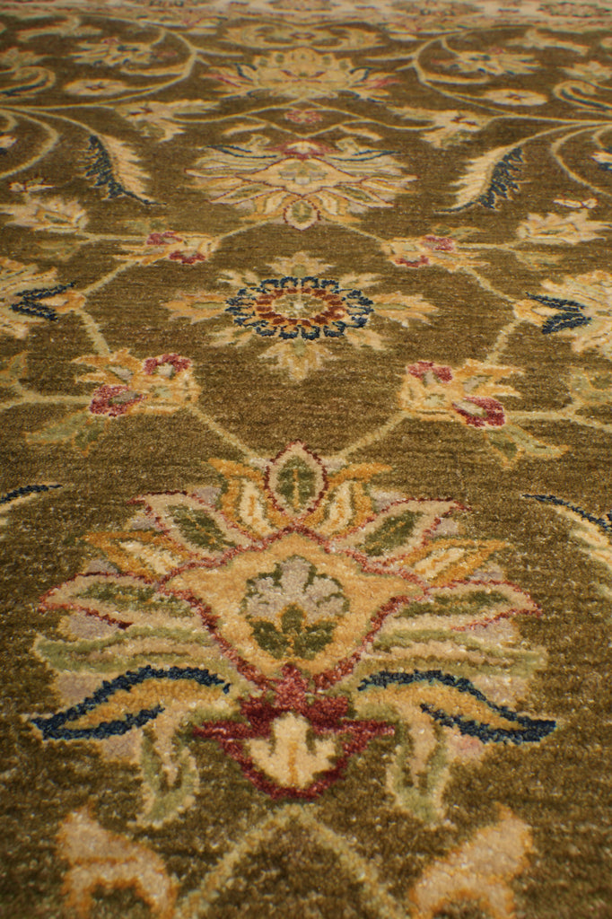 A close-up of an ornate traditional area rug with a floral and vine pattern in olive green, beige, blue, and red.