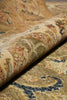 Load image into Gallery viewer, A close-up of a rolled section of an ornate area rug showing its detailed vintage-style pattern in beige, gold, brown, and navy blue.