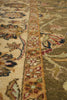 Load image into Gallery viewer, Close-up of an ornate area rug with a central floral pattern, featuring a cream field, a beige border, and olive green sections with blue and red accents.