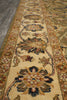 Load image into Gallery viewer, A close-up view of a traditional patterned area rug with a cream center field, floral motifs, and a warm brown and beige border, shown on a dark wood floor.
