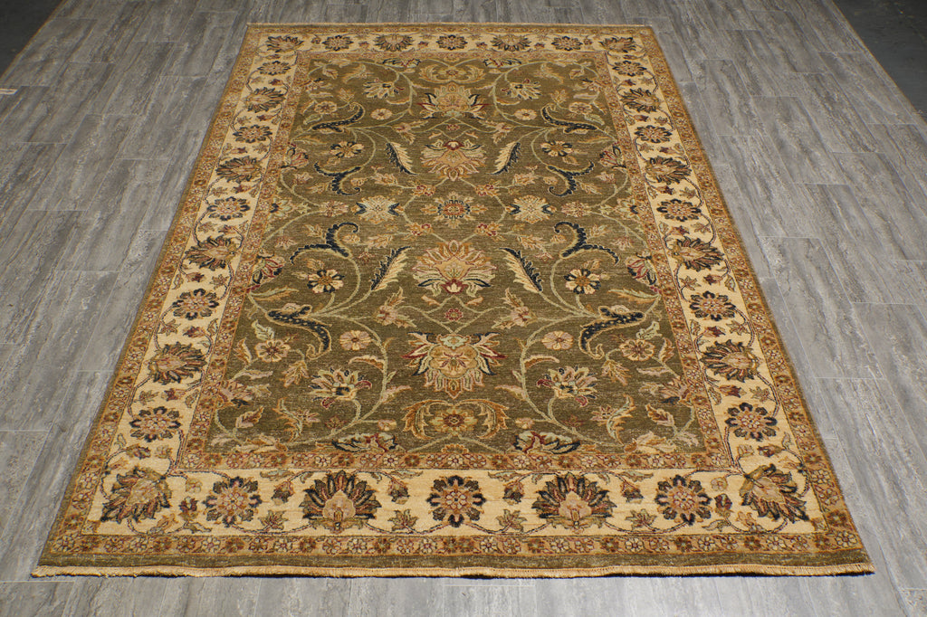An ornate rectangular area rug with a traditional floral and vine pattern, laid out on a gray wood-look floor. The rug features a dominant olive green center field, a beige border, and accents of brown, blue, and gold in the intricate floral motifs.