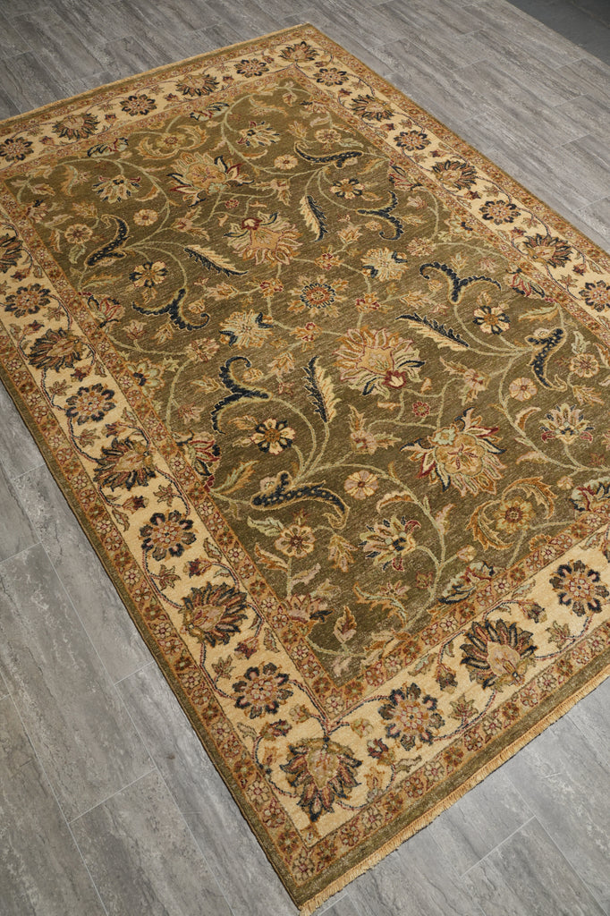 An oriental-style area rug with an intricate floral and vine pattern, shown from an elevated angle on a gray wood-look floor. The rug features a dominant olive green center, a beige border, and accents of brown, gold, and blue.