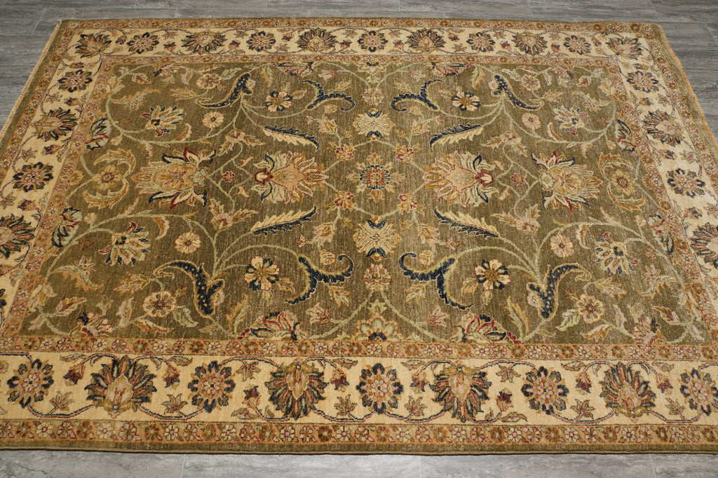 An ornate rectangular area rug with a traditional floral and vine pattern, featuring a warm olive-green center field, beige borders, and accents of navy blue, rust red, and cream, laid out on a gray tiled floor.