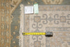 Load image into Gallery viewer, A close-up of an area rug with a beige and gray traditional pattern, showing the fringed edge, a yellow tape measure, and two tags on a neutral background.