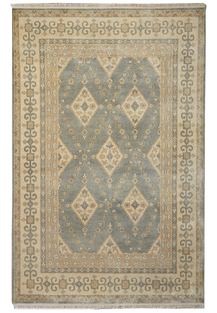 A rectangular area rug with a traditional geometric pattern in muted blue-gray, beige, and cream tones, featuring a central diamond motif and ornate border details.