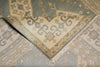 Load image into Gallery viewer, A close-up of a folded area rug showing its traditional pattern and fringed edge. The rug features a muted sage green, beige, and light blue-gray color palette with intricate floral and scroll motifs.