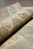 Load image into Gallery viewer, Close-up of a rolled area rug showing a traditional pattern in beige, gray, and muted blue-green tones.