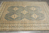 Load image into Gallery viewer, A rectangular area rug with a traditional geometric pattern in muted sage green, beige, and brown tones, laid out on a dark wood floor.