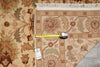 Load image into Gallery viewer, A close-up of a patterned area rug with a beige base and floral motifs in brown, rust, and muted green, shown with a yellow tape measure and price tag on a gray floor.