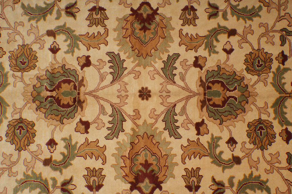A close-up of an ornate floral patterned fabric or rug with a cream background and motifs in tan, olive green, and dark brown.