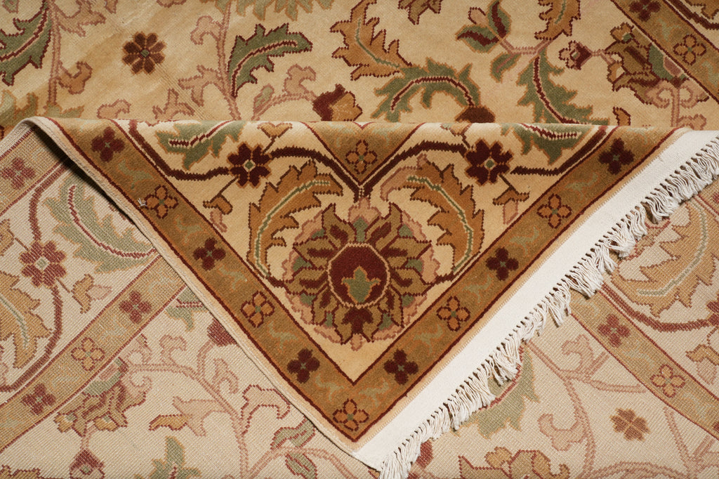A close-up of a patterned area rug with cream, tan, brown, and muted green floral motifs and white fringe along one corner.