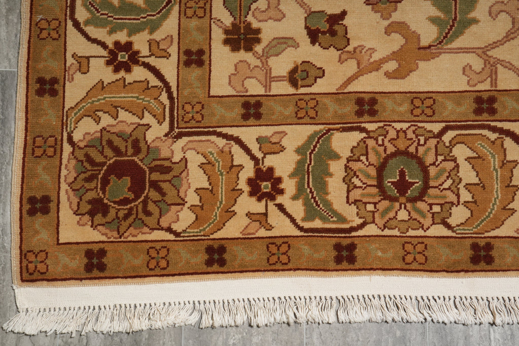 A close-up of a traditional patterned rug showing its cream and beige base, brown floral motifs, green accents, and white fringe at the bottom.