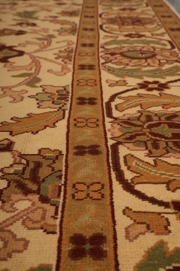 Close-up of a patterned area rug with a beige background and traditional floral motifs in brown, green, and muted orange.