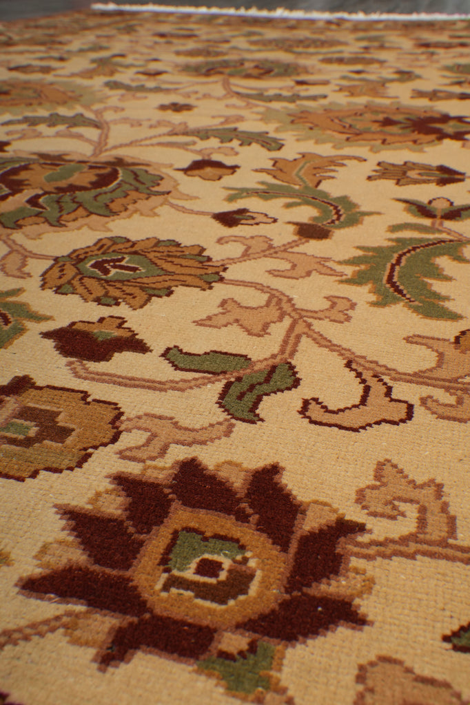 Close-up of a woven rug with an ornate floral pattern in beige, brown, green, and muted orange tones.