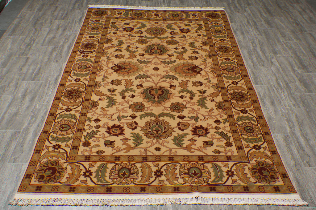 A rectangular traditional area rug with an intricate floral and medallion pattern, laid flat on a gray wood-look floor. The rug features a beige center field, a warm brown border, and cream fringe on the bottom edge.