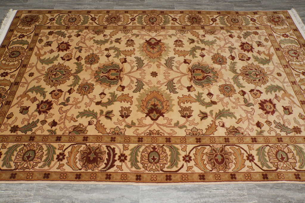 An ornate rectangular area rug with a traditional floral and medallion pattern, featuring a beige background with brown, green, and rust-red motifs, laid out on a gray tiled floor.