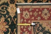 Load image into Gallery viewer, A folded area rug with a traditional floral pattern, showing a red field, beige borders, and a dark green outer section. A yellow tape measure lies horizontally across the fold to indicate size, and a white product tag is attached near the top left corner.
