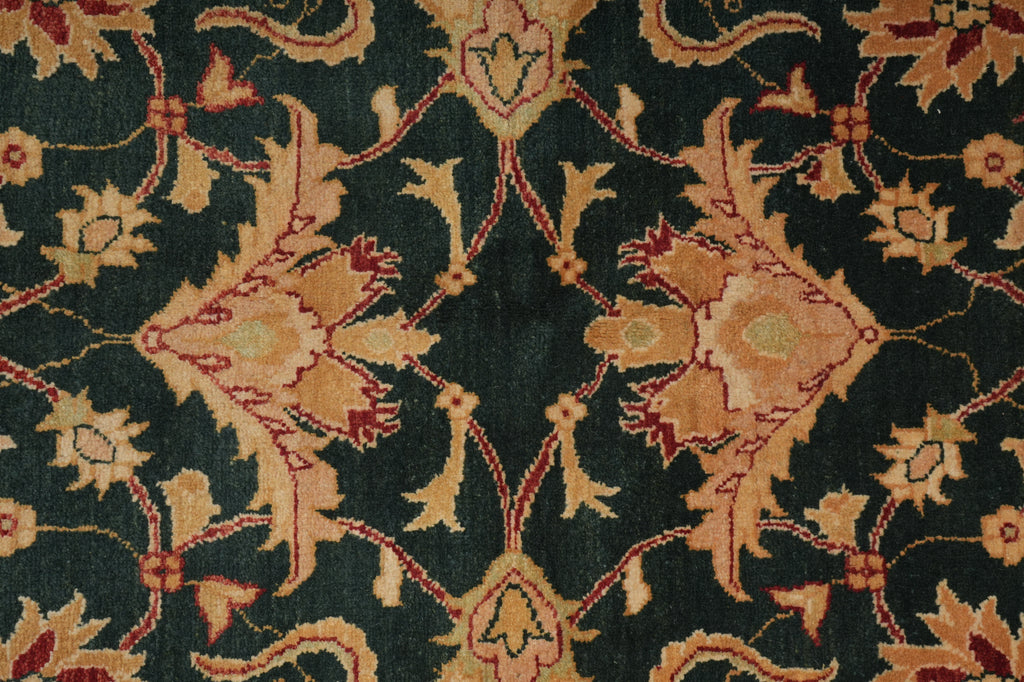 A close-up of an ornate floral patterned rug with a dark green background and beige, tan, and muted red motifs.
