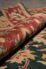 Load image into Gallery viewer, A close-up of a folded area rug showing its detailed traditional pattern in red, beige, and dark green.