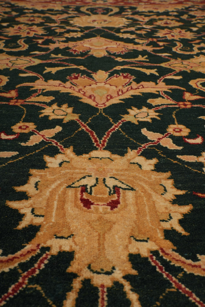 A close-up of a traditional patterned area rug with a dark green background, beige central medallion, and red and gold floral details.