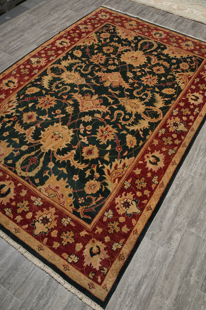 A traditional oriental-style area rug with a dark green central field, red borders, and beige floral motifs, shown laid out on a gray wood-look floor.