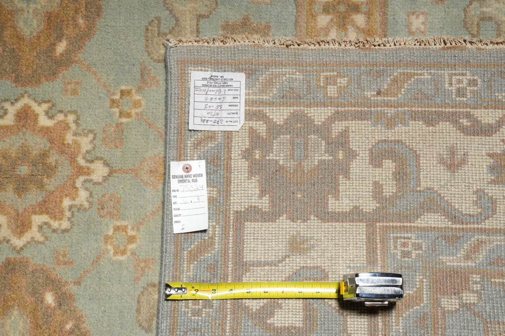 A patterned area rug shown with a tape measure and inventory tags on a matching rug surface, likely documenting size and condition.