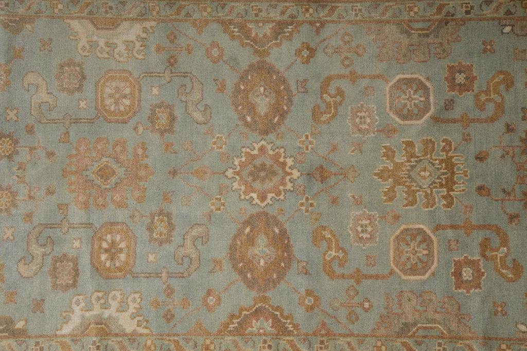 A close-up of a traditional patterned rug with a dusty blue-gray background and warm brown, beige, and muted gold motifs.