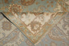 Load image into Gallery viewer, A close-up of a traditional patterned area rug with a folded corner showing its cream-colored inner side and detailed botanical motifs in muted blue, beige, and brown.