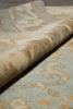 Load image into Gallery viewer, Close-up of a patterned area rug with a rolled corner showing the pile and border design in beige, cream, and muted blue tones.