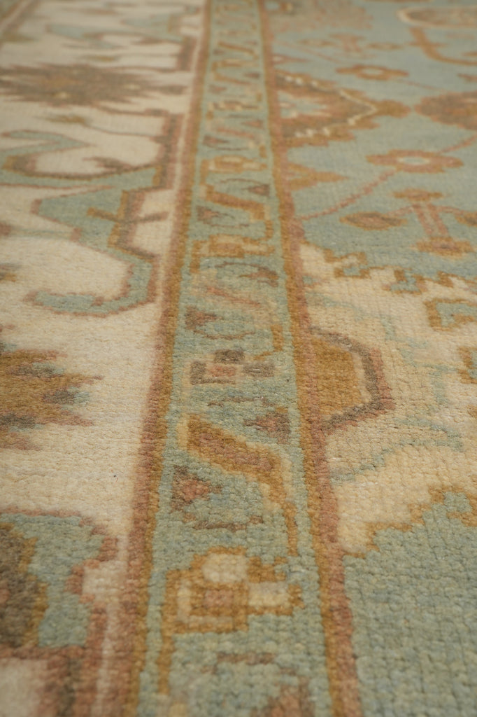 Close-up of a patterned area rug showing a detailed woven design in muted shades of beige, light blue, and brown.