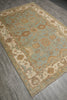 Load image into Gallery viewer, An ornate rectangular area rug with a traditional floral and medallion pattern, shown laid out on a gray wood-look floor. The rug features a dusty sage green center field, beige borders, and warm brown accents.