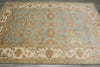 Load image into Gallery viewer, A rectangular area rug with a traditional medallion and floral pattern in muted sage green, beige, and brown tones, laid flat on a dark gray floor.