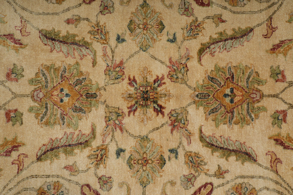 A close-up of an ornate traditional rug with a beige background and intricate floral and vine patterns in muted green, rust red, and blue.