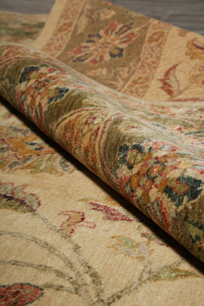 A close-up of a rolled area rug showing its detailed traditional floral pattern in beige, brown, green, and muted red tones.