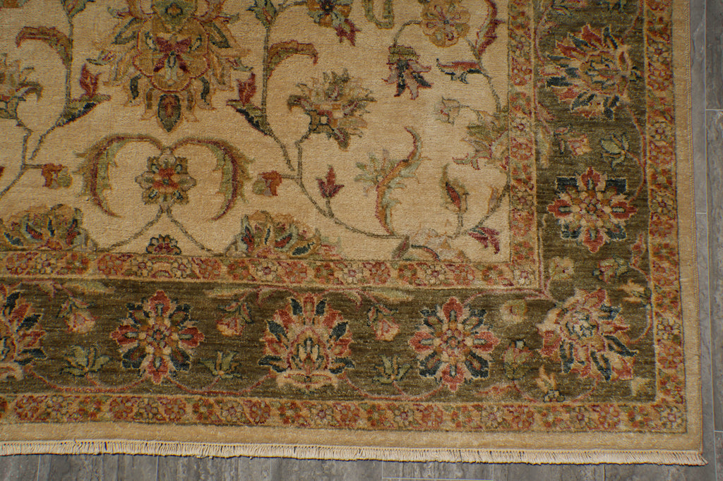 A close-up of a traditional oriental rug showing its corner, featuring a beige central field with floral motifs and a dark olive green border with red and blue accents.