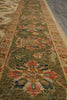 Load image into Gallery viewer, A close-up view of an ornate area rug with a traditional floral pattern in olive green, beige, rust red, and blue, shown laid out on a gray floor.