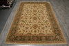 Load image into Gallery viewer, A rectangular traditional area rug with an ornate floral and vine pattern, laid out on a gray wood-plank floor. The rug features a beige center field surrounded by green and brown borders with detailed floral motifs.