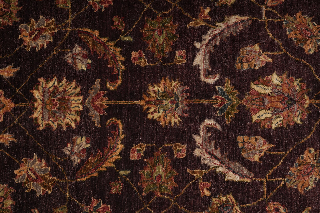 A close-up of an ornate traditional rug pattern with floral and paisley motifs on a very dark brown or near-black background, featuring warm beige, rust red, and muted green accents.