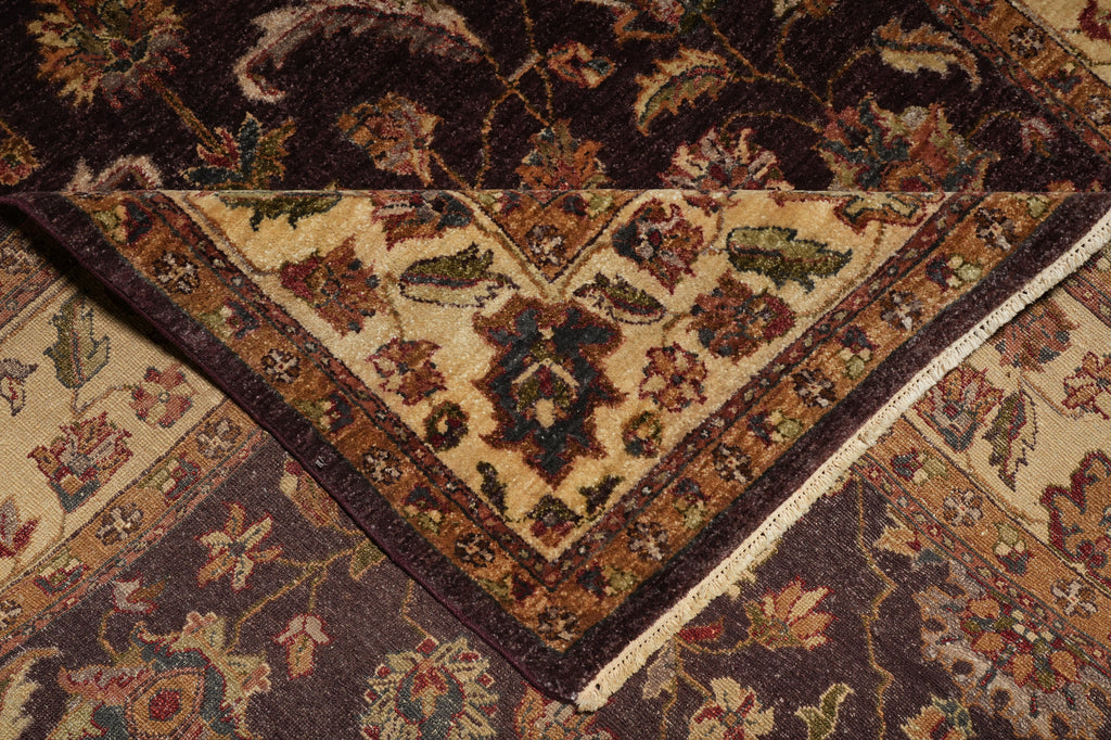 A close-up of an ornate traditional area rug with a folded corner revealing its cream center and dark brown floral borders, layered over another similar rug.