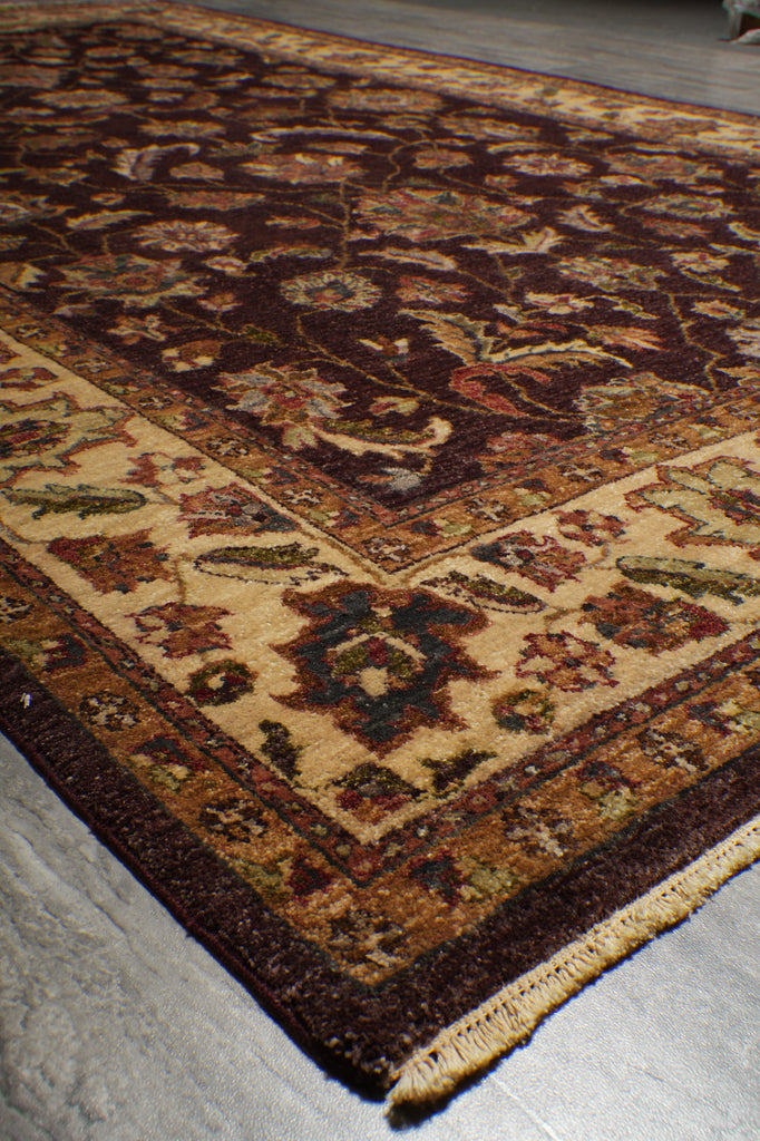 A close-up view of an oriental area rug with a traditional floral pattern, featuring a dark brown border, beige center, and red, green, and blue accents.