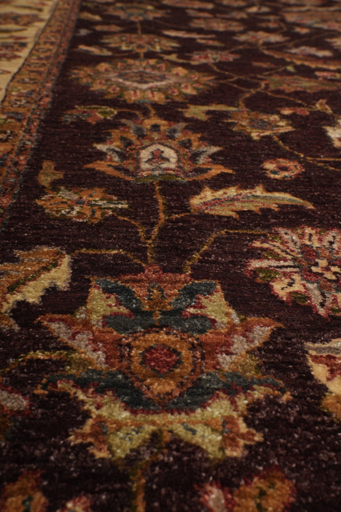 Close-up of a traditional patterned rug with a dark brown background and floral motifs in beige, green, and rust tones.