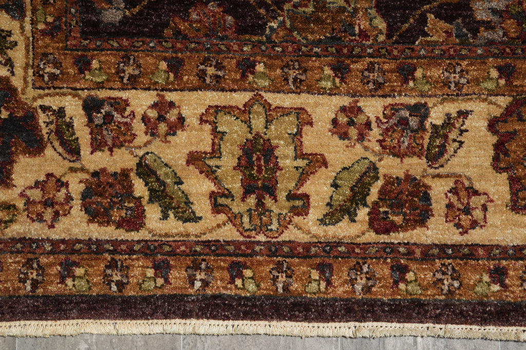 Close-up of an ornate patterned rug showing a central floral medallion and border motifs in beige, brown, burgundy, green, and muted gold tones.