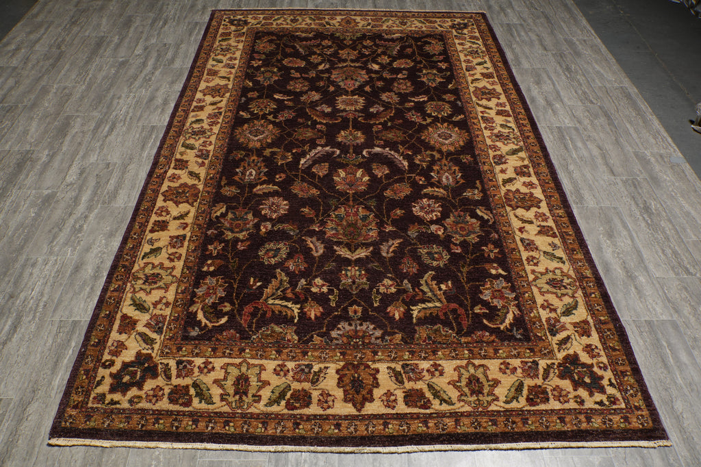 A rectangular traditional area rug with an intricate floral pattern, featuring a dark brown center, beige borders, and red accents, laid out on a gray wood-look floor.