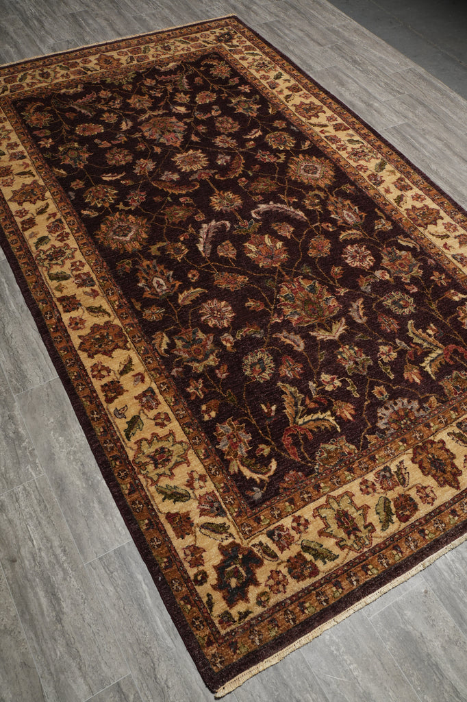 A rectangular traditional area rug with an intricate floral pattern, featuring a dark brown center, beige borders, and multicolored details, laid out on a gray wood-look floor.