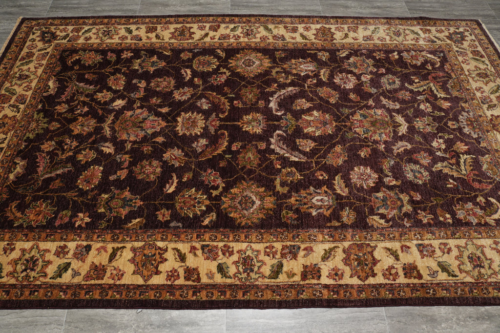 A rectangular traditional area rug with an intricate floral and vine pattern, featuring a dark brown center field and beige borders, laid out on a gray tiled floor.